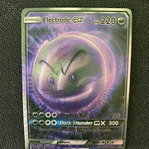 May include: A holographic Pokemon trading card featuring Electrode GX from the Shadow series. The card is green and purple with a black border. The card has a picture of Electrode GX and the text "Shadow Ball 120" and "Dark Thunder GX 300".