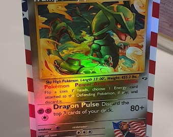 Può includere: Una carta da gioco di Pokemon olografica che presenta Rayquaza, un Pokemon simile a un drago verde con occhi rossi. La carta è un Pokemon base con 230 HP e ha un potere chiamato "Orgoglio americano". La carta è su uno sfondo di una bandiera americana.
