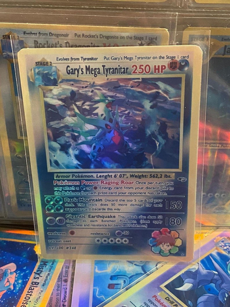 May include: A blue and red Pokemon card featuring Gary's Mega Tyranitar. The card has a holographic finish and shows the Pokemon in a battle pose. The card text includes the Pokemon's name, HP, and attacks. The card is from the Pokemon Trading Card Game.