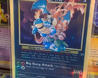 Op de afbeelding: Een holografische Pokémon-kaart met het Kanto Starter Trio: Bulbasaur, Charmander en Squirtle. De kaart is blauw en goud met een zwarte rand. De naam van de kaart is "Oak's Kanto Starter Trio" en het heeft 350 HP. De aanval van de kaart is "Big Bang Attack" en het doet 50 schade aan zichzelf.