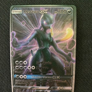 May include: A holographic Pokemon card featuring Mewtwo GX, a powerful psychic Pokemon with a dark purple and blue color scheme. The card has a HP of 300 and features attacks like Earthquake and Psywave. The card also has a Shadow Vortex GX attack.