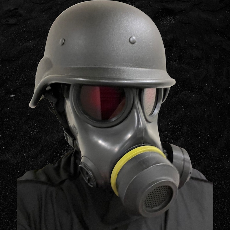 Puede incluir: Una m&aacute;scara de gas negra con un casco negro y una correa amarilla. La m&aacute;scara de gas tiene una visera de color rojo.