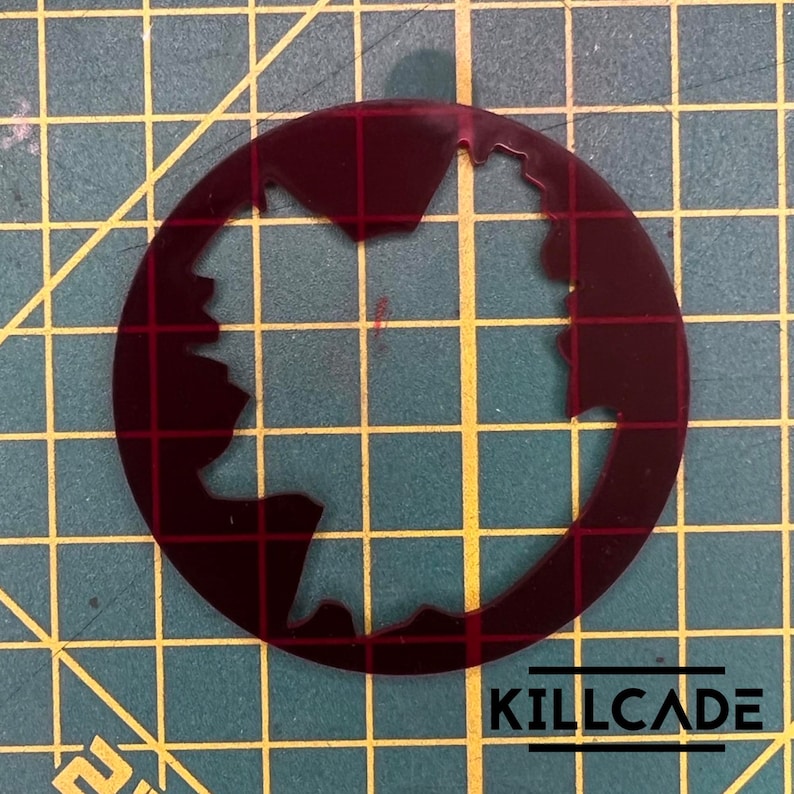 Puede incluir: Una plantilla circular de color rojo oscuro con una forma irregular y dentada recortada en el centro. La plantilla est&aacute; sobre un fondo de cuadr&iacute;cula verde.