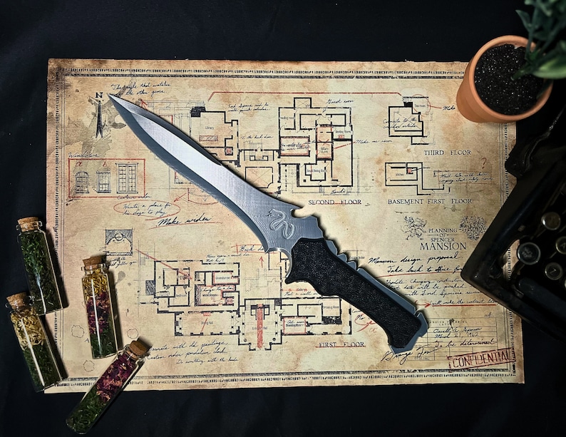 May include: A silver knife with a black handle lies on a vintage map with a floor plan of a mansion. The map is labeled "Planning of Spencer Mansion".