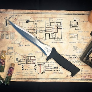 May include: A silver and black tactical knife with a serrated blade and a black handle. The knife is lying on a map with a floor plan of a mansion. The map is labeled "Planning of Spencer Mansion".