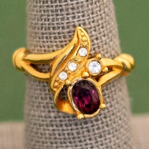 Può includere: Anello in oro con una pietra preziosa viola e strass trasparenti in un design a foglia.