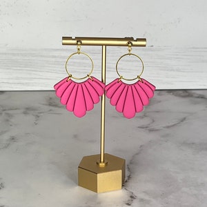 May include: A pair of pink fan-shaped earrings with gold hoops. The earrings are displayed on a gold stand.