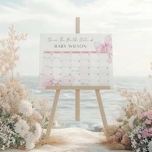 Op de afbeelding: Een roze en witte kalender met een strik aan de voorkant. De kalender staat op een ezel en zegt "Raad de geboortedatum van Baby Wilson".