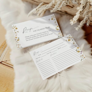 Puede incluir: Dos tarjetas de recetas blancas con dise&ntilde;os florales. La tarjeta superior tiene el texto "Receta para la novia" e instrucciones para escribir una receta favorita. La tarjeta inferior es una plantilla de receta en blanco con secciones para "De", "Tiempo de preparaci&oacute;n", "Tiempo de cocci&oacute;n", "Porciones", "Ingredientes" y "Instrucciones".