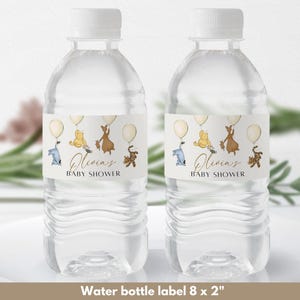 May include: Two clear plastic water bottles with labels featuring Winnie the Pooh characters. The labels are white with brown text that reads "Olivia's Baby Shower". The characters are flying with balloons.