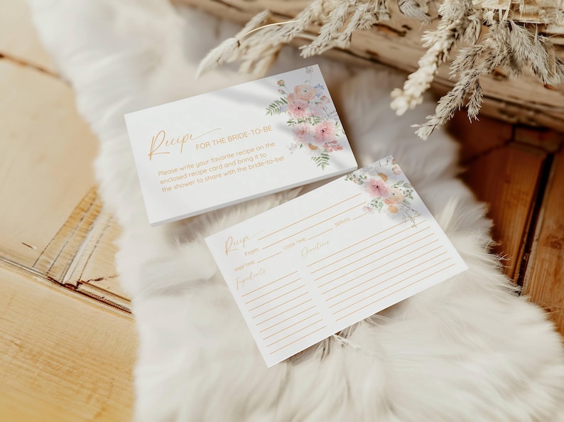 Op de afbeelding: Twee witte receptenkaarten met bloemenontwerpen. De bovenste kaart zegt "Recept voor de bruid" en vraagt ​​gasten om hun favoriete recepten op de meegeleverde receptenkaart te schrijven en deze mee te nemen naar de bruiloft om te delen met de bruid.