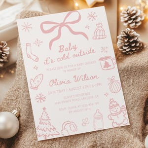 May include: A light pink baby shower invitation with the text "Baby it's cold outside." The invitation includes illustrations of winter-themed items like snowflakes, mittens, and a snowman. The details include the date, time, and location.