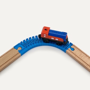 May include: A toy train set featuring a red and blue locomotive on a blue curved track. The track connects to a wooden track, creating a playful scene. The train has black wheels and white accents.