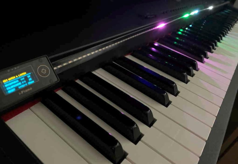 Peut inclure: Un clavier de piano num&eacute;rique noir dot&eacute; de touches blanches et noires avec une bande lumineuse LED int&eacute;gr&eacute;e au-dessus des touches. Un petit panneau de commande rectangulaire sur la gauche affiche le texte i-Piano et un menu num&eacute;rique bleu.