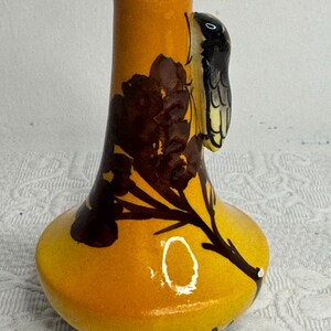 May include: A ceramic vase with a glossy yellow and orange gradient finish, featuring a dark brown painted floral branch design and a three-dimensional black and white insect figure attached to the side of the neck of the vase.