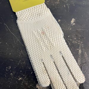 May include: A vintage white mesh glove with a yellow tag attached. The tag reads "GANT EXTENSIBLE POUR TOUTES TAILLES - DAME -". The glove has a diamond pattern and is likely made of a delicate material.