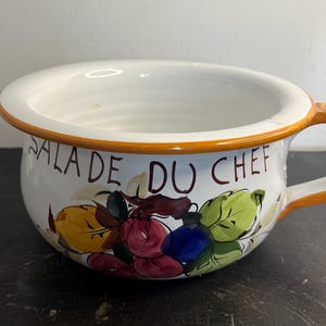 Peut inclure: Bol à salade en céramique blanche avec un bord et une poignée orange. Le bol est décoré de fruits colorés et des mots "SALADE DU CHEF". Le bol est conçu pour servir des salades.