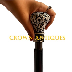 May include: A black walking stick with a white and black patterned handle. The handle has a silver band with rhinestones. The text "CROWN ANTIQUES" is visible in the image.