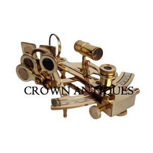 Könnte beinhalten: Ein Messing-Sextant mit mehreren Linsen, Zifferblättern und einem kleinen Teleskop. Das Instrument hat eine polierte Goldoberfläche und der Text "CROWN ANTIQUES" ist auf der Vorderseite aufgedruckt.