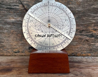 May include: A silver-toned circular protractor with a wooden base. The protractor has a compass rose, numbers, and letters around the edge. The text "CROWN ANTIQUES" is printed on the protractor.