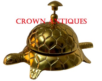 May include: A gold-coloured turtle-shaped service bell with a domed top. The bell has a textured shell design and a small knob on top.