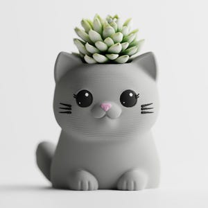 Może przedstawiać: Szara doniczka w kształcie kota z rośliną sukulentową. Doniczka ma duże czarne oczy, różowy nos i czarne wąsy. Kot siedzi z łapami z przodu. Sukulent jest zielony i ma wiele liści.