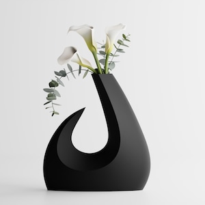Puede incluir: Un jarrón negro moderno con un diseño curvo único. Contiene calas blancas y ramas de eucalipto verdes, creando un contraste llamativo. Un elemento de decoración del hogar elegante.