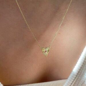 May include: A gold chain necklace with a small, round, white stone pendant. A second gold chain necklace with a textured heart pendant featuring a small red stone in the center.