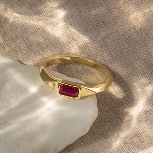 May include: A gold ring with a rectangular ruby gemstone set in the centre.