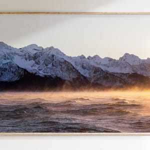 May include: A photograph of a snow-capped mountain range in the distance with a misty, golden sunrise over a choppy sea.