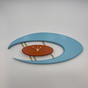 May include: A wall clock featuring a large, light blue, crescent-shaped frame surrounding a smaller, solid, oval-shaped, rust-colored center piece. The center piece is connected to the frame by four thin, gold-toned metal rods and has gold clock hands.