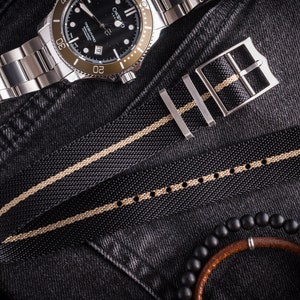 May include: A black and beige striped watch strap with a silver buckle. The strap is made of a woven nylon material.