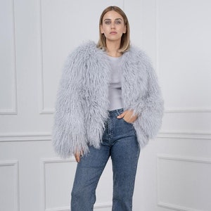 May include: A woman wearing a light gray fluffy jacket, blue jeans, and black platform shoes.