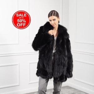 May include: A black fur coat with a large collar. The model is wearing grey jeans and black heeled boots. A red circle with the text "SALE UP TO 50% OFF" is in the top left corner of the image.