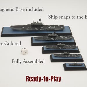 Op de afbeelding: Een verzameling voorgekleurde, volledig geassembleerde model oorlogsschepen op magnetische bases. De schepen zijn van verschillende groottes en staan op blauwe platforms met zwarte randen. De tekst is zichtbaar.