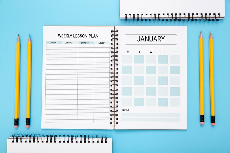 May include: A white planner with a black spiral binding. The left page has a weekly lesson plan section with the headings "Subject" repeated four times. The right page has a calendar for January with the days of the week labeled M, T, W, T, F. There is a section labeled "Notes" at the bottom of the page. Two yellow pencils are on a light blue background.