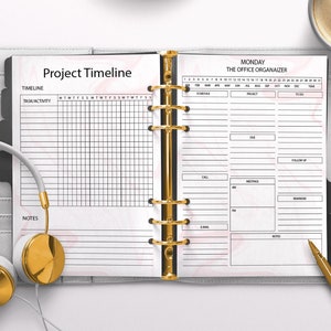 May include: A white planner with a gold ring binder. The left page has the title "Project Timeline" and a grid for scheduling tasks. The right page has the title "Monday The Office Organizer" and a grid for scheduling appointments, calls, meetings, and emails.