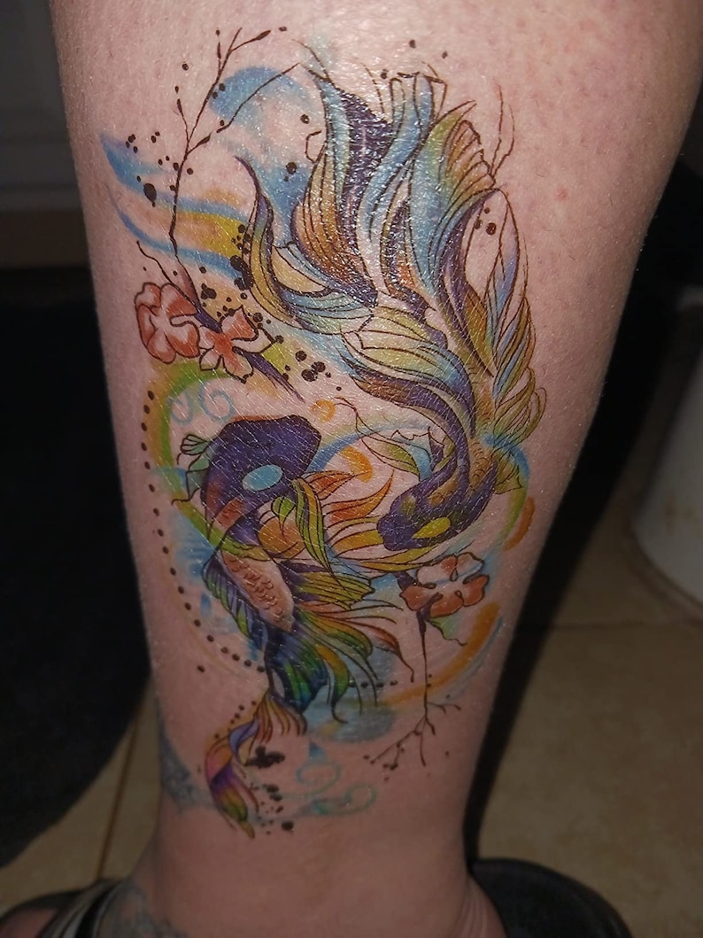 May include: A colorful temporary tattoo of a fish with watercolor-like details. The fish is surrounded by flowers and swirls.
