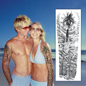 May include: A couple with temporary tattoos on their arms. The tattoos are black and white and feature a clock, an eye, and a building. The tattoos are on their upper arms and extend to their elbows.