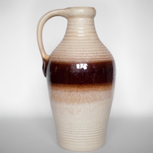 Pode incluir: Um jarro de cerâmica marrom e branco com uma boca larga e uma alça. O jarro tem uma faixa marrom ao redor do meio e um esmalte branco.