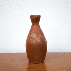 Może przedstawiać: Mały, brązowy ceramiczny wazon o zaokrąglonym korpusie i wąskiej szyjce. Wazon ma marmurkową glazurę w odcieniach brązu, pomarańczy i bieli.