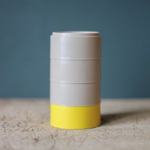 Peut inclure: Un ensemble de quatre contenants ronds empilés, avec une base jaune et un dessus beige. Les contenants sont posés sur une surface en bois.