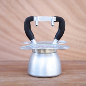 Pode incluir: Uma cafeteira de espresso de aço e preto com um design de alça único. A cafeteira tem uma base redonda e uma parte superior plana com dois bicos.