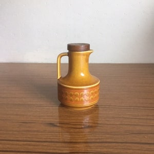 May include: A brown ceramic oil and vinegar bottle with a wooden lid. The bottle has a decorative pattern of small circles.