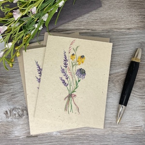 May include: A blank card with a watercolor illustration of a bouquet of wildflowers. The flowers are purple, yellow, and pink. The card is made of recycled paper and has a rustic look.