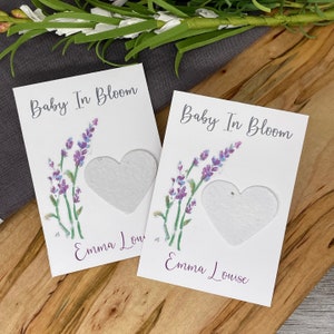 May include: Two white cards with lavender flowers and a heart-shaped seed paper insert. The text on the cards reads "Baby In Bloom" and "Emma Lou".