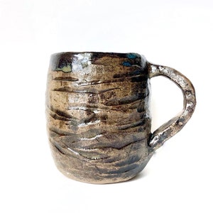 May include: A brown ceramic mug with a textured, wavy surface and a dark brown glaze. The mug has a rounded body and a handle.