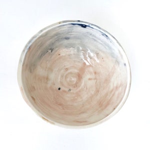 May include: A white ceramic bowl with a light pink and blue glaze. The bowl has a swirling pattern and a glossy finish.