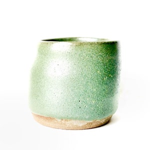 May include: A green ceramic mug with a speckled glaze. The mug has a rounded shape and a slightly flared lip.