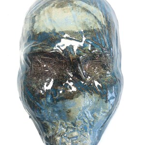 May include: A ceramic mask with a blue and brown glaze. The mask has a human-like face with a textured surface.